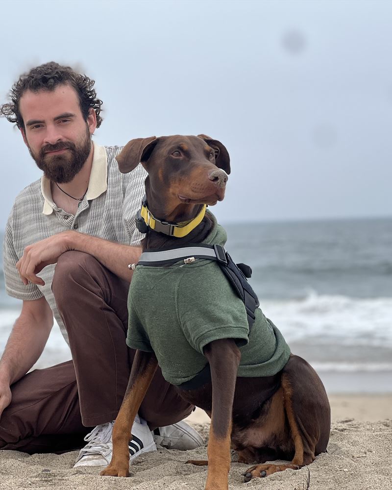 Matt Gilbert kneeling on the beach with his Doberman